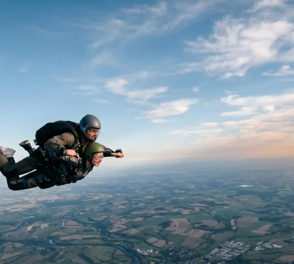 Tandem skydiving pair exiting aircraft at high altitude with expansive sky and cloud formations